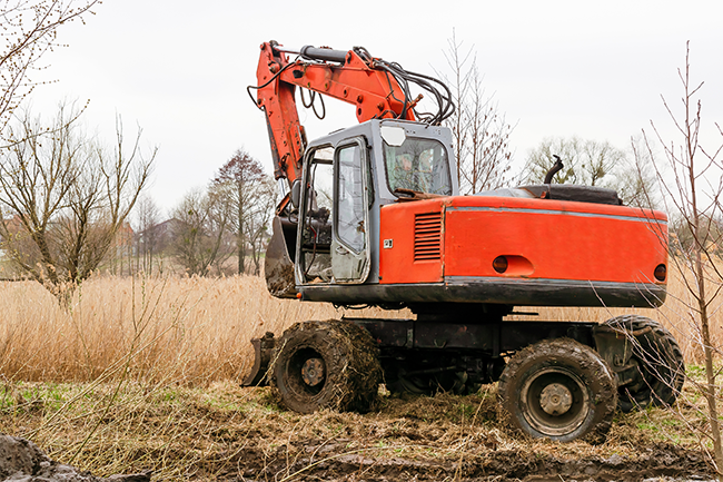 Photo of a red excavator in a muddy field.